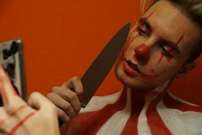 Person with artistic makeup holding a knife and a phone, illustrating the impact of Photoshop on beautiful photos.