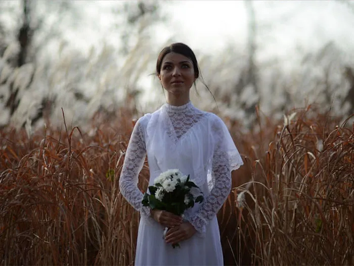 Woman in lace white dress holding flowers, standing in a field, illustrating the truth behind beautiful photos before Photoshop.