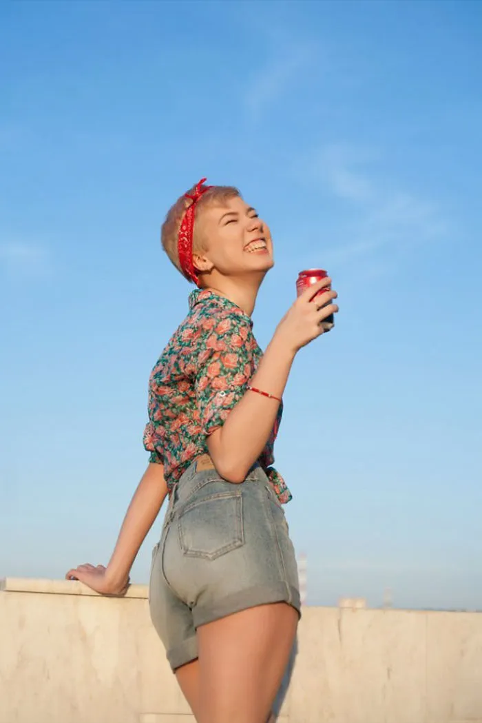 Person enjoying a sunny day, smiling with a drink in hand, demonstrating "before Photoshop" natural beauty.