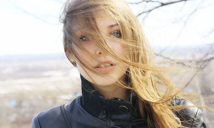 Woman with windblown hair in a black jacket, showcasing natural beauty before Photoshop.