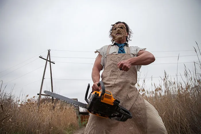 Man wearing a mask and apron, holding a chainsaw outdoors, showcasing dramatic transformation before and after Photoshop.