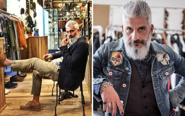 Stylish older man with gray hair, seated in a clothing store, wearing a dark jacket and casual pants; redefining handsome.