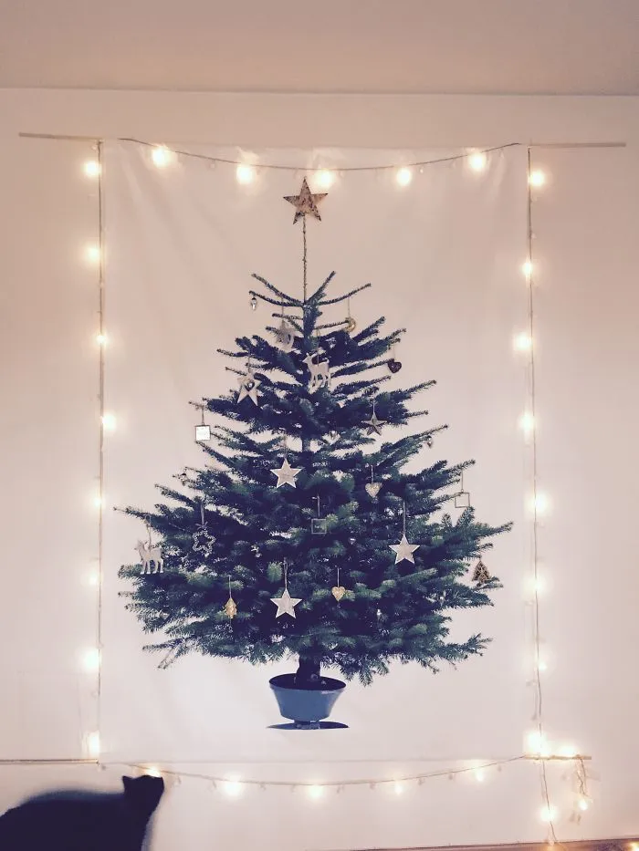 Wall-mounted Christmas tree protected from pets with holiday lights.