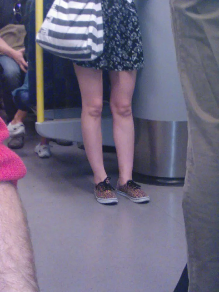 Woman standing in crowded subway, floral dress and striped bag, with surprise detail to notice.