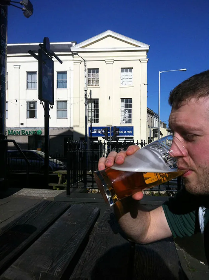 Man drinking beer with building in background, hidden detail visible.
