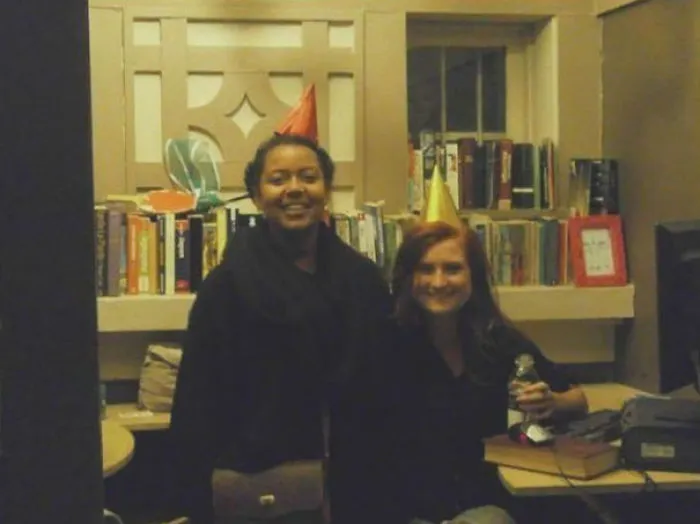 Two people wearing party hats in a study room, smiling with books in the background; a hidden detail might freak you out.