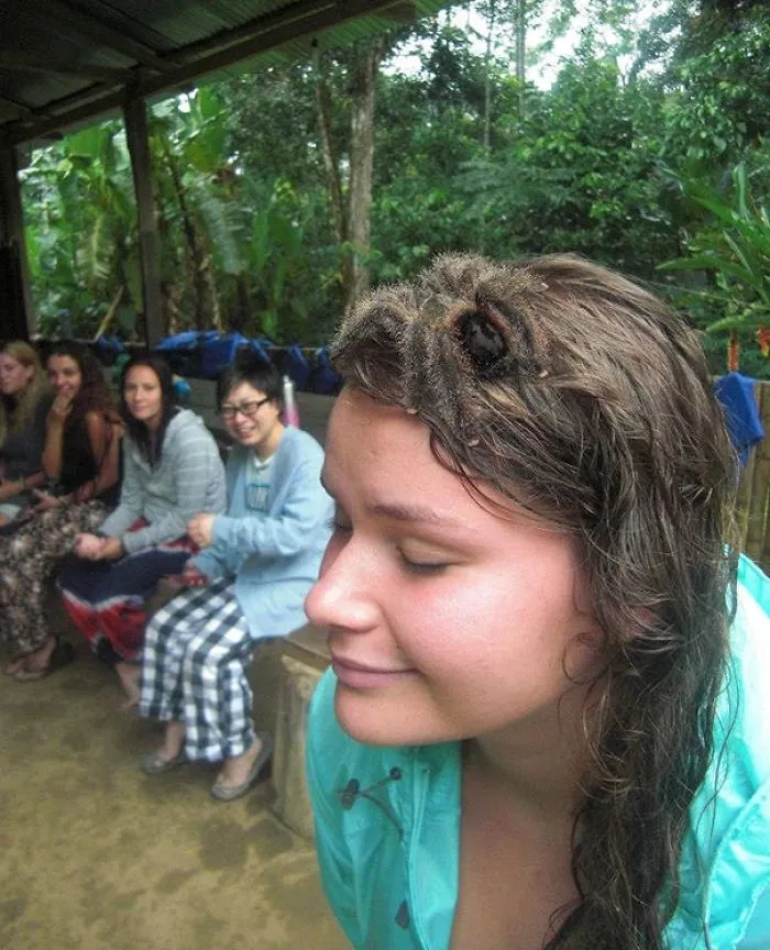 A girl with a tarantula on her head, smiling in a group setting, evoking a surprising reaction when you see it.