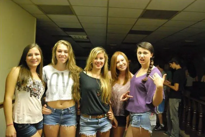 Five smiling friends posing indoors; unexpected detail in the background.