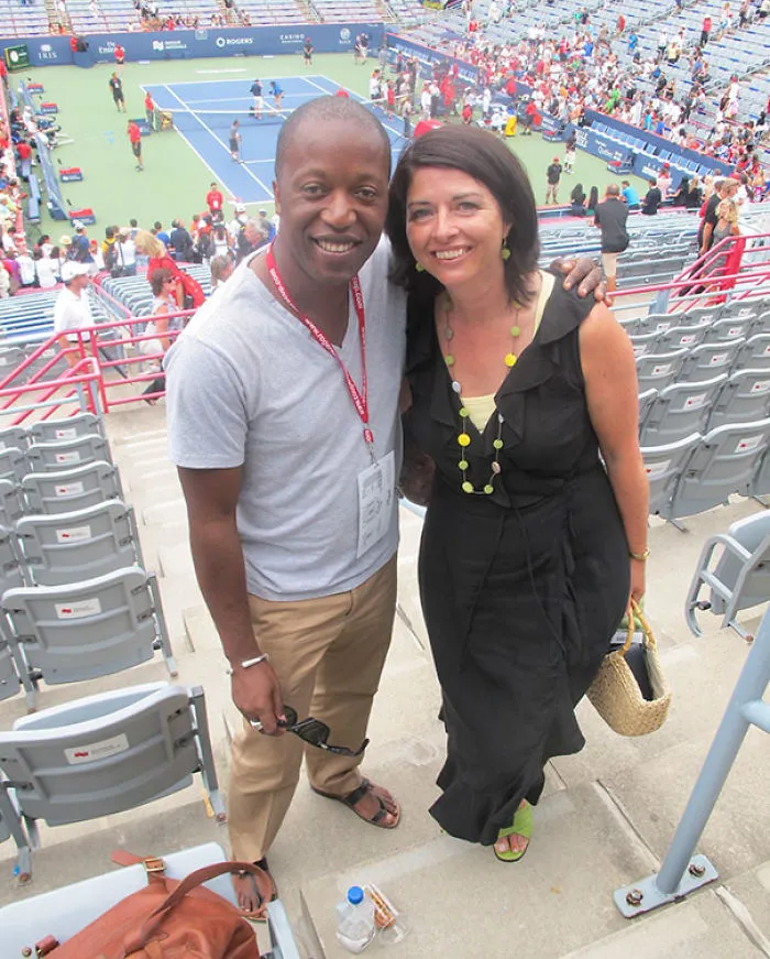 Two people smiling at a tennis event, surrounded by a crowd in the stands. Can you spot what's unusual in this image?