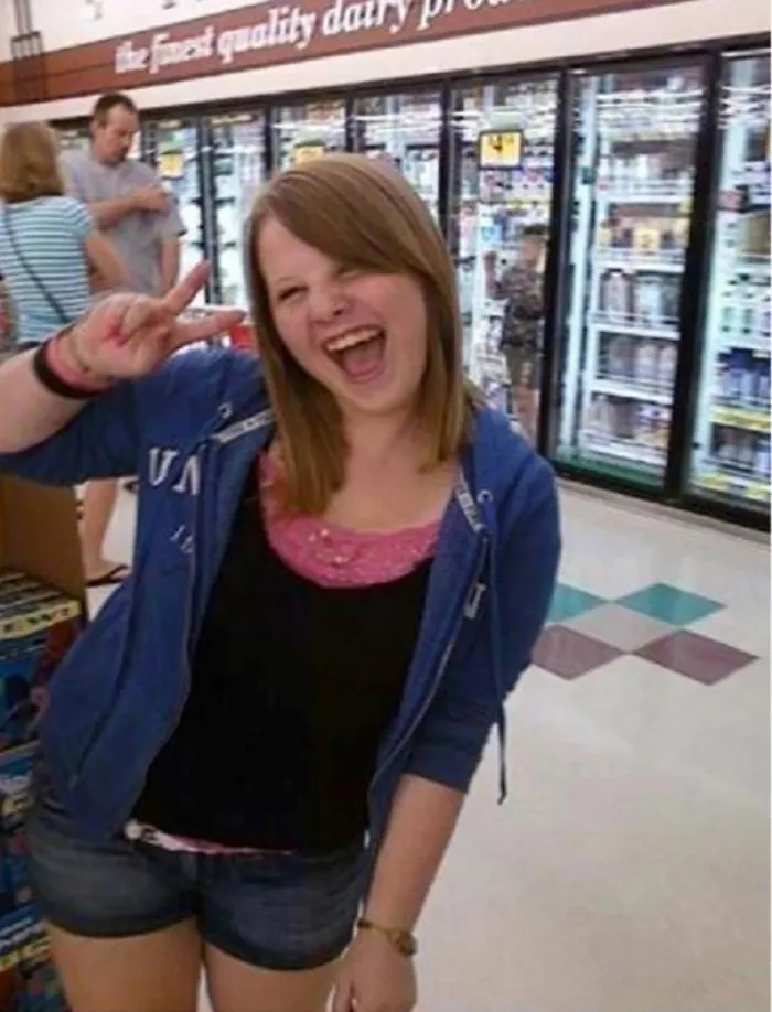 Smiling girl posing with peace sign in a grocery store aisle, an unexpected detail in the background might freak you out.