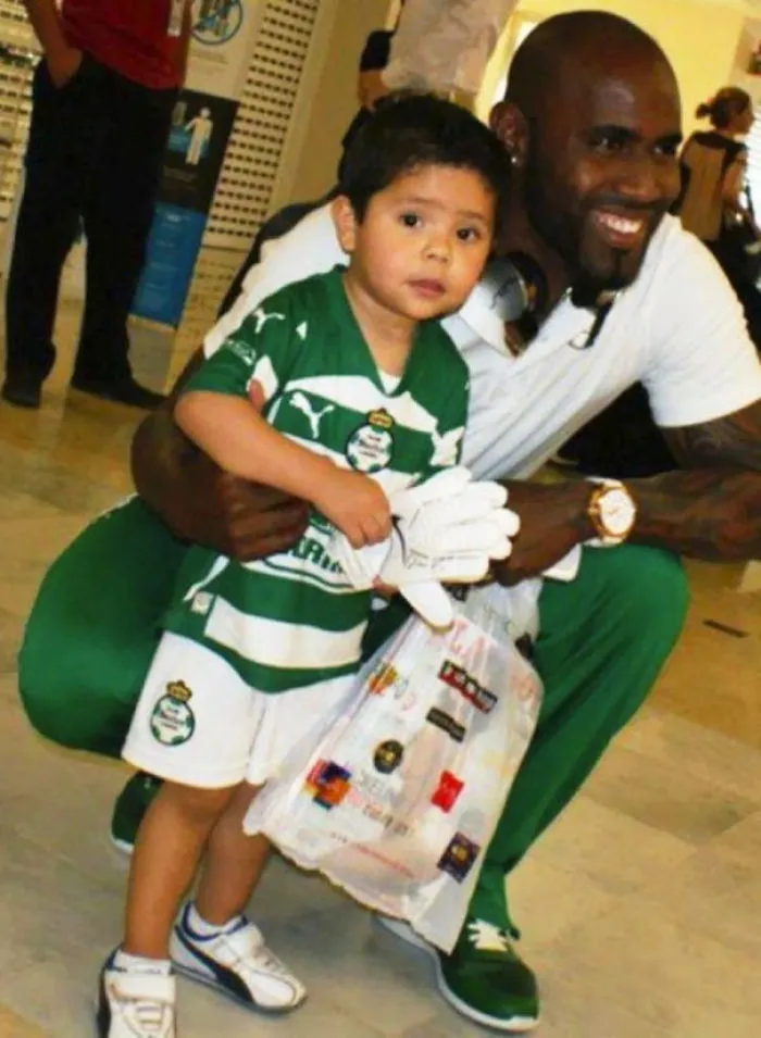 Young boy in a green sports uniform stands next to a smiling man, holding a plastic bag, creating a "when you see it" effect.