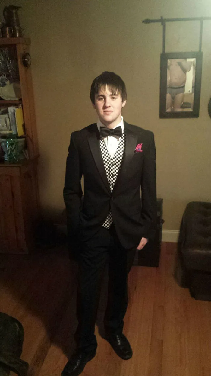 Young man in a tuxedo, standing indoors; surprising detail in the background mirror.