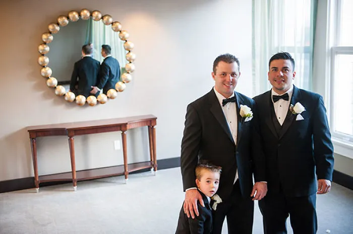 Two men in tuxedos with a child, their reflection missing in the mirror on the wall behind, creates an eerie effect.