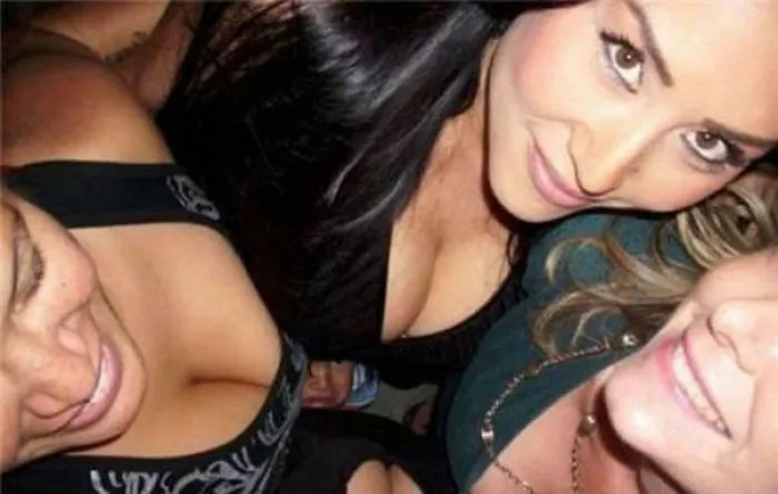 Three women smiling closely for a selfie, an unexpected detail is subtly hidden.