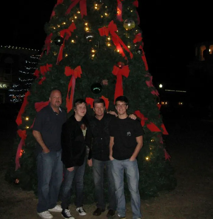 Four people standing in front of a decorated Christmas tree at night, with a surprise hidden detail to freak you out.
