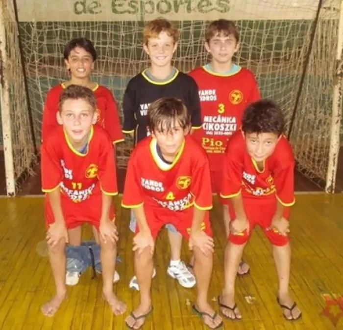 Youth soccer team posing in red uniforms, standing on a gym court with a goal net in the background.