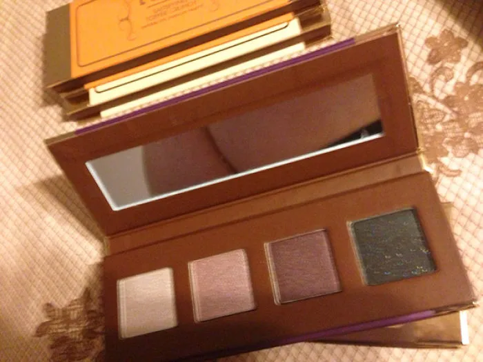 An eyeshadow palette on a bed with a hidden reflection in the mirror.