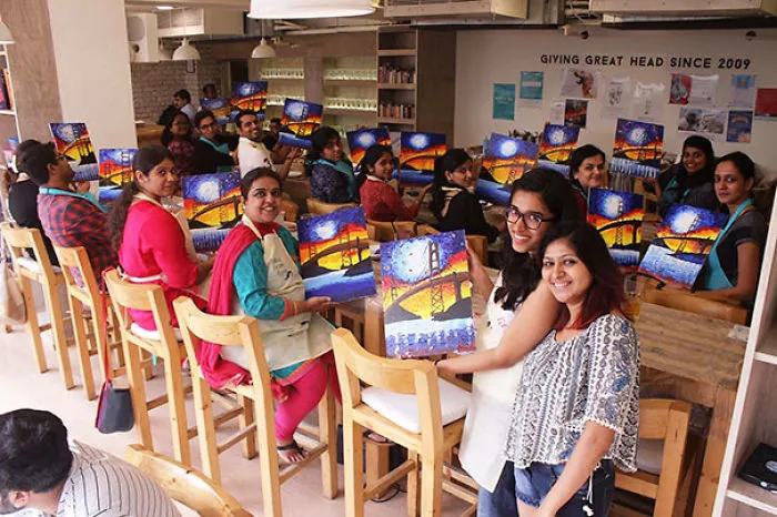 Group of people in a room proudly displaying colorful paintings.