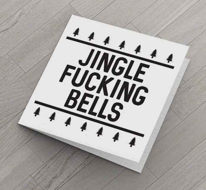 Rude Christmas card on a wooden floor with text "Jingle Fucking Bells" and tree decorations.