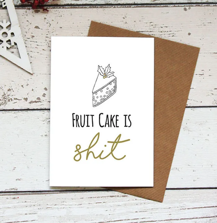 Rude Christmas card with fruitcake illustration and humorous message on wooden background.