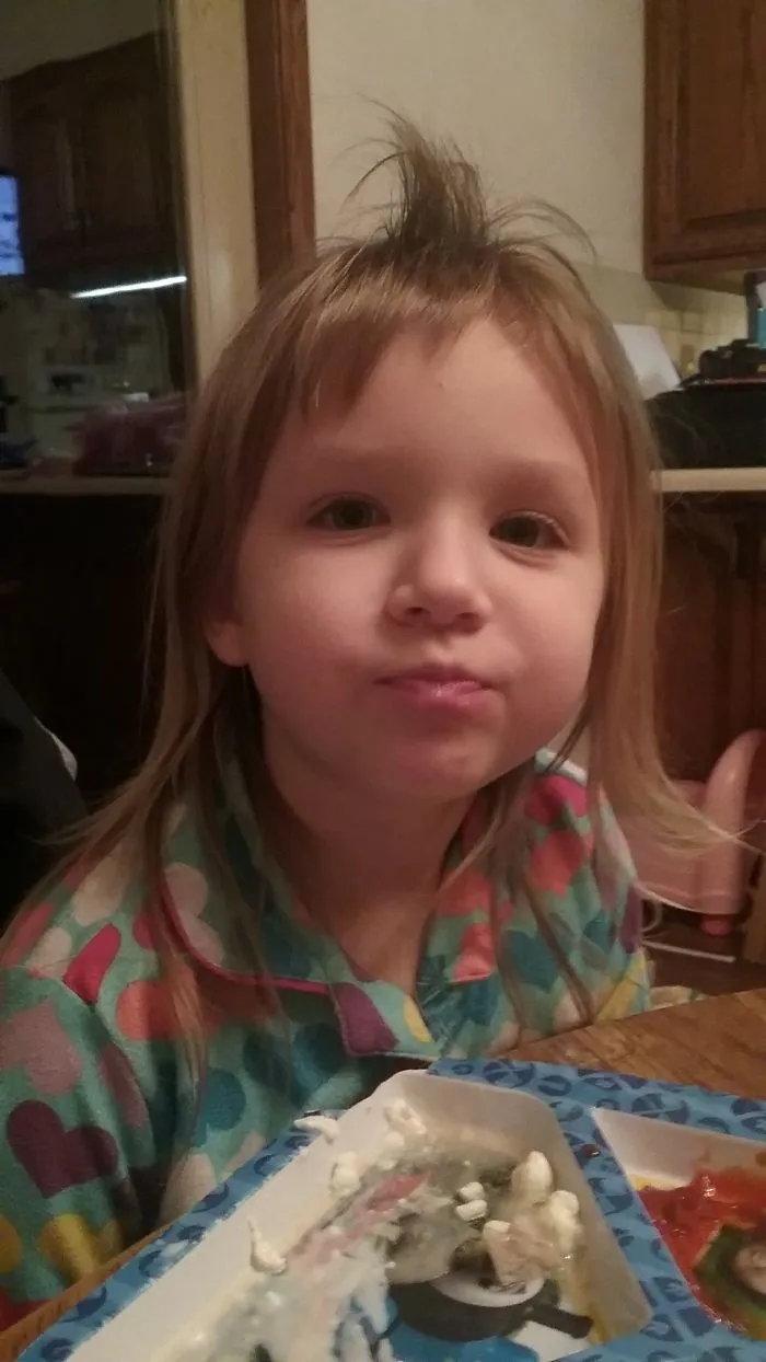 Toddler with a self-cut hairstyle sits at a table, wearing a colorful heart-patterned pajama top.