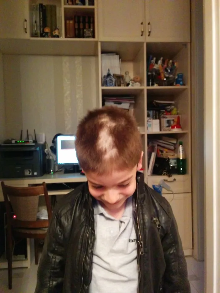 Child with uneven haircut looking down, wearing a black jacket, highlighting kids' hair cutting mishap.