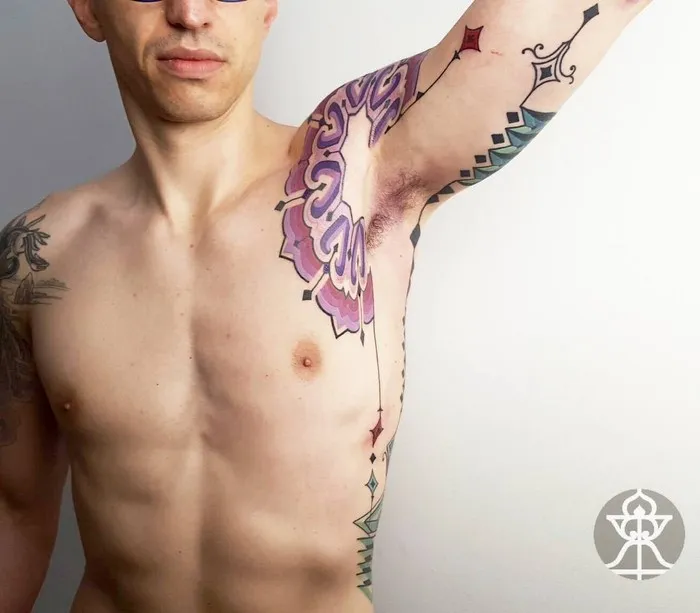 Man with intricate Amazonian tribal tattoo by Brazilian artist on arm and chest, showcasing vibrant colors and patterns.