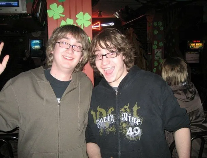 Two strangers with similar features smiling in a lively bar setting, showcasing a real-life doppelganger moment.
