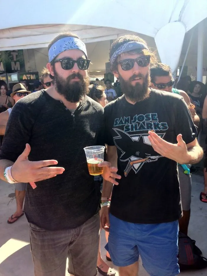 Two men wearing sunglasses and bandanas at a festival, discovered as real-life doppelgangers.