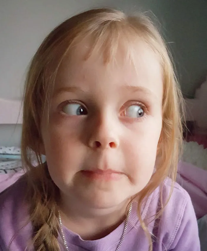 Child with uneven bangs showing regret after a self haircut, wearing a purple sweater and making a funny expression.