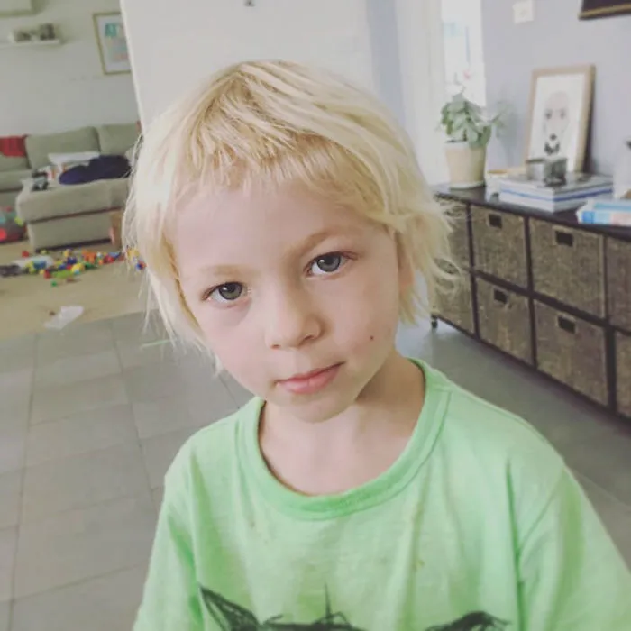Young child with a self-cut hairstyle, looking serious in a casual home setting.