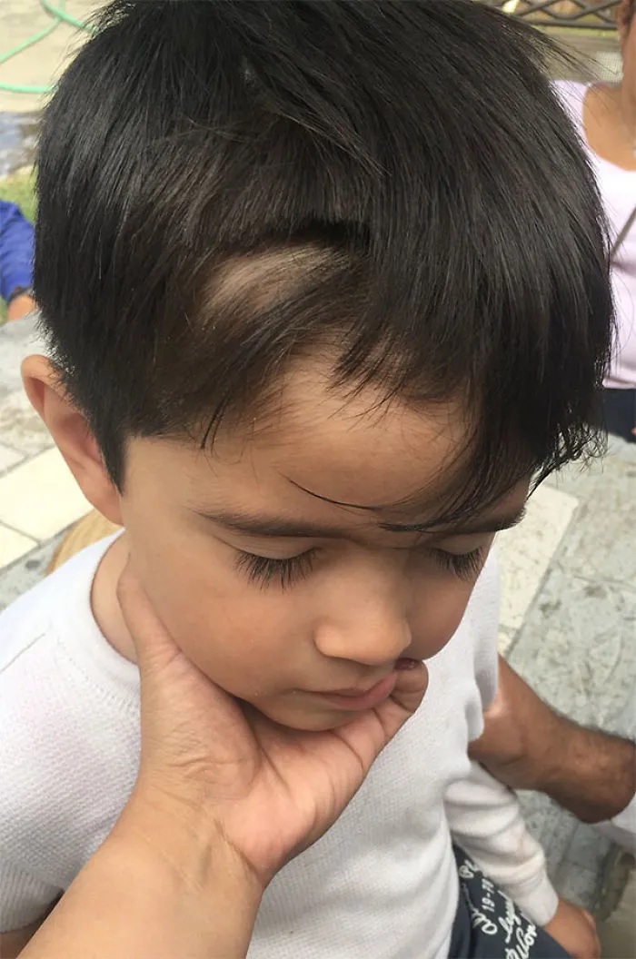 Child with uneven haircut, evidence of self haircut attempt, looking down with an adult's hand on their cheek.