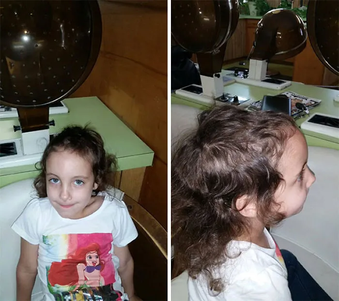 Child showing uneven haircut, sitting in a salon chair, wearing a shirt with a mermaid print.