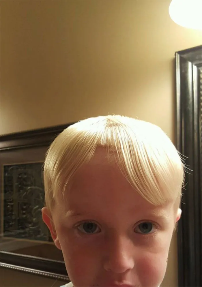 Child with self-cut bangs, looking at the camera, in a bathroom setting.