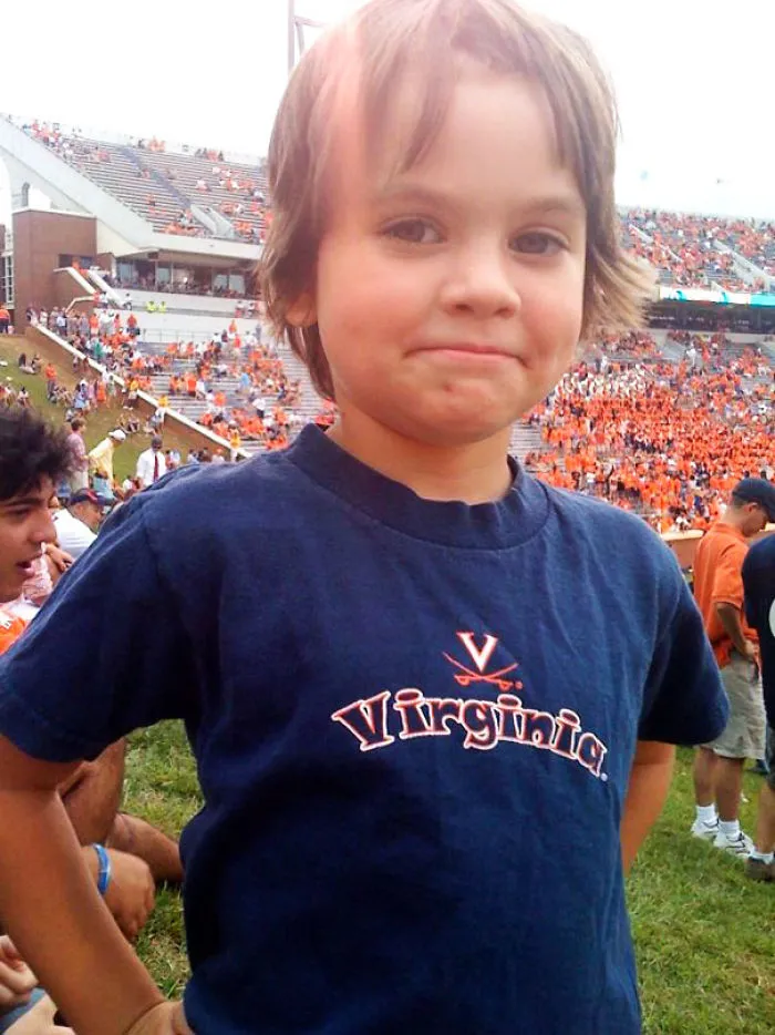 Child with self-cut hair, wearing a Virginia shirt, smiling at a sports event.