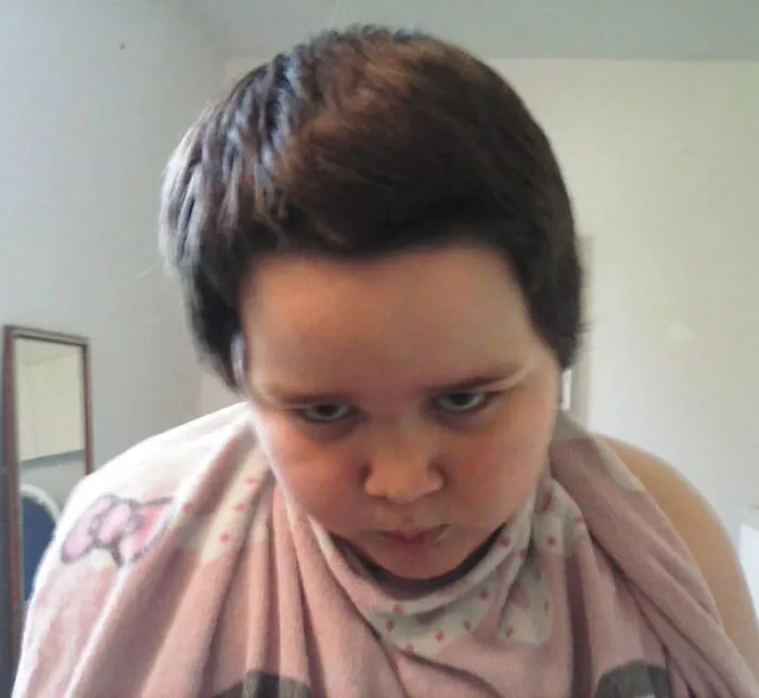 Child with a self-cut hairstyle looks displeased, wearing a patterned towel.