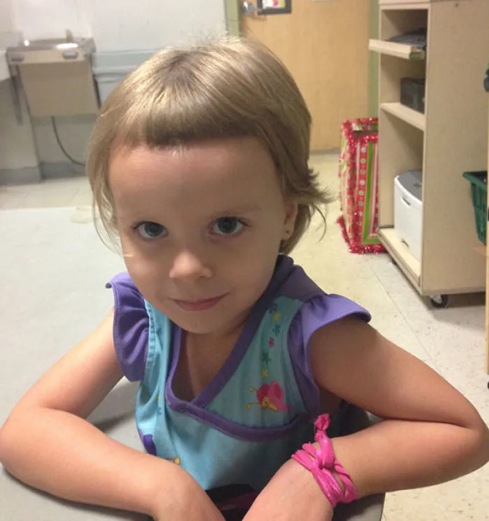 Child with a self-cut hairstyle, sitting at a table, wearing a colorful dress, shows playfulness and curiosity.