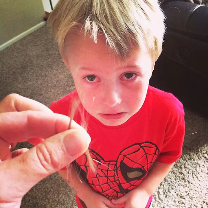 Child looking regretful after cutting own hair, wearing a red Spider-Man shirt.