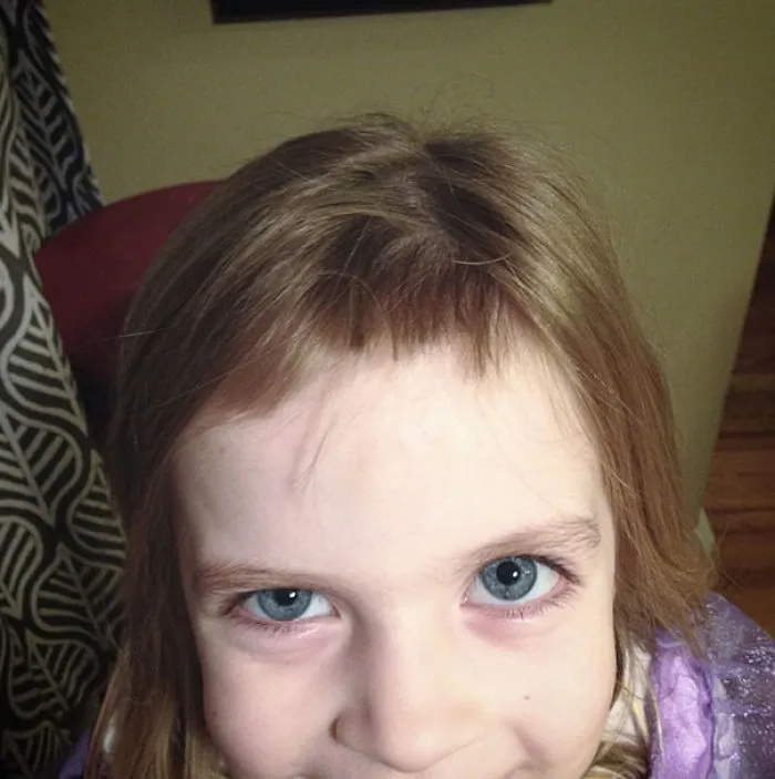 Child with uneven bangs after cutting their own hair, smiling innocently.