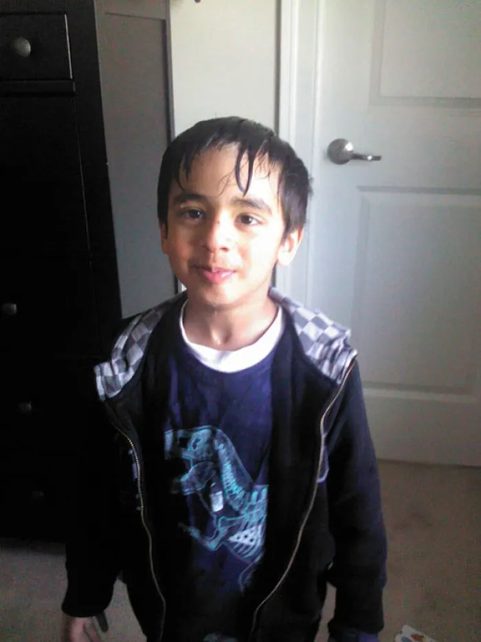 Child with a self-cut hairstyle, standing indoors, smiling slightly with wet hair strands on forehead.