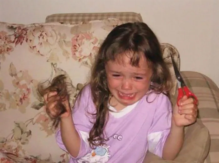 Child holding scissors and hair, looking upset after a self haircut decision.