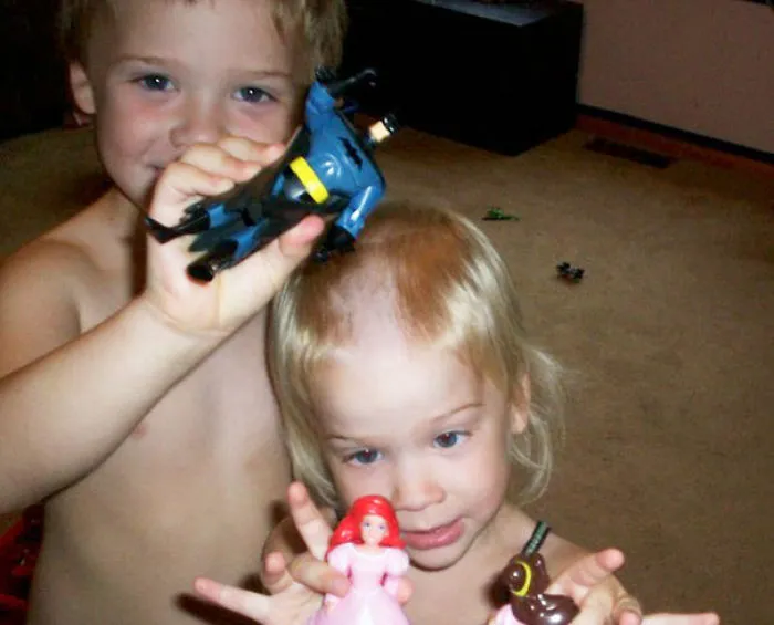 Two kids playing, one with a self-cut haircut holding toys, highlighting a DIY hair cutting decision.