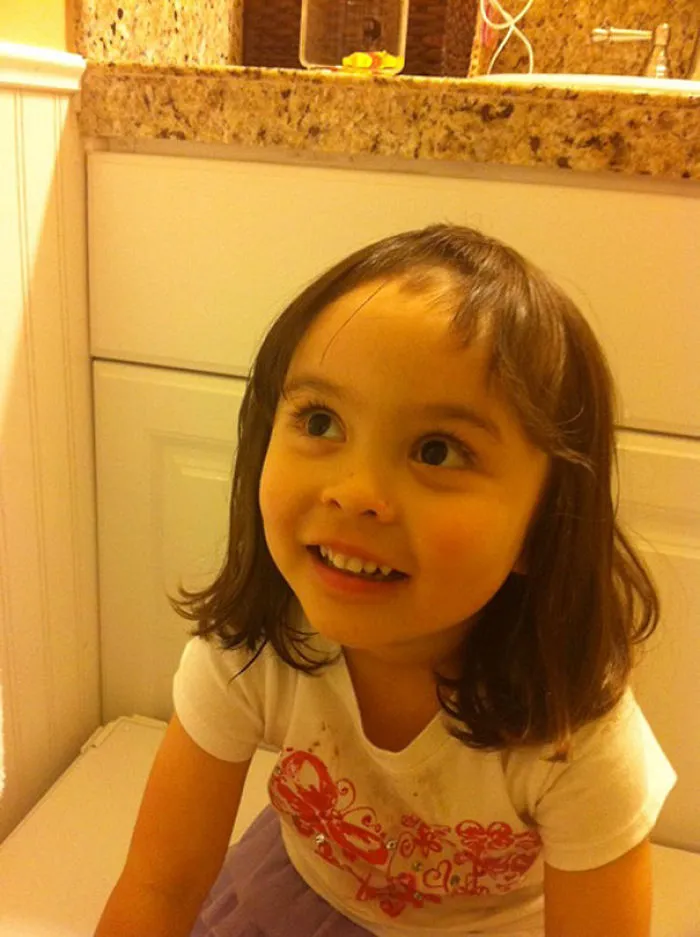 Child with uneven bangs, smiling after attempting a haircut.