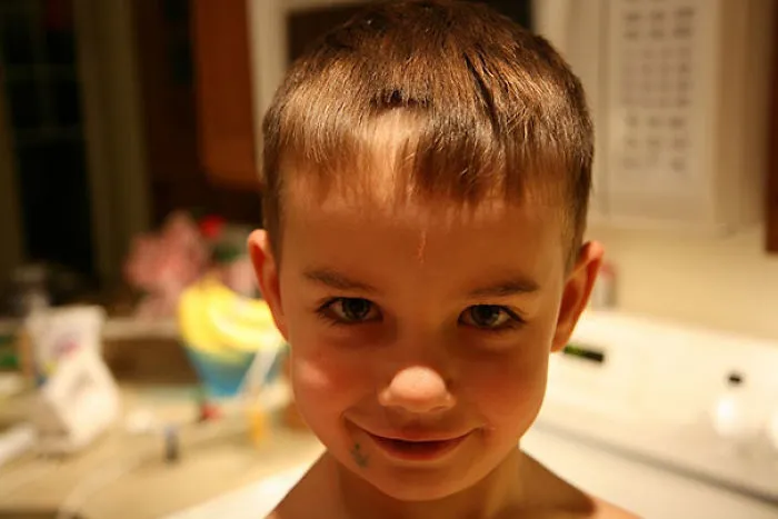 Child with self-cut hair, smiling in a kitchen setting.