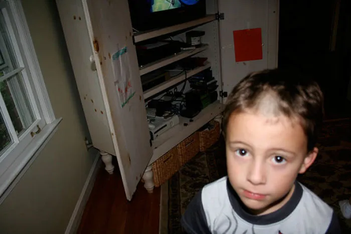Child with a self-inflicted haircut stands in a living room, appearing regretful about the decision.