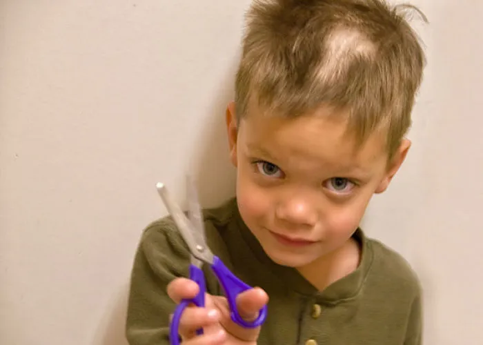 Child holding scissors with a self-cut uneven haircut, looking regretful.
