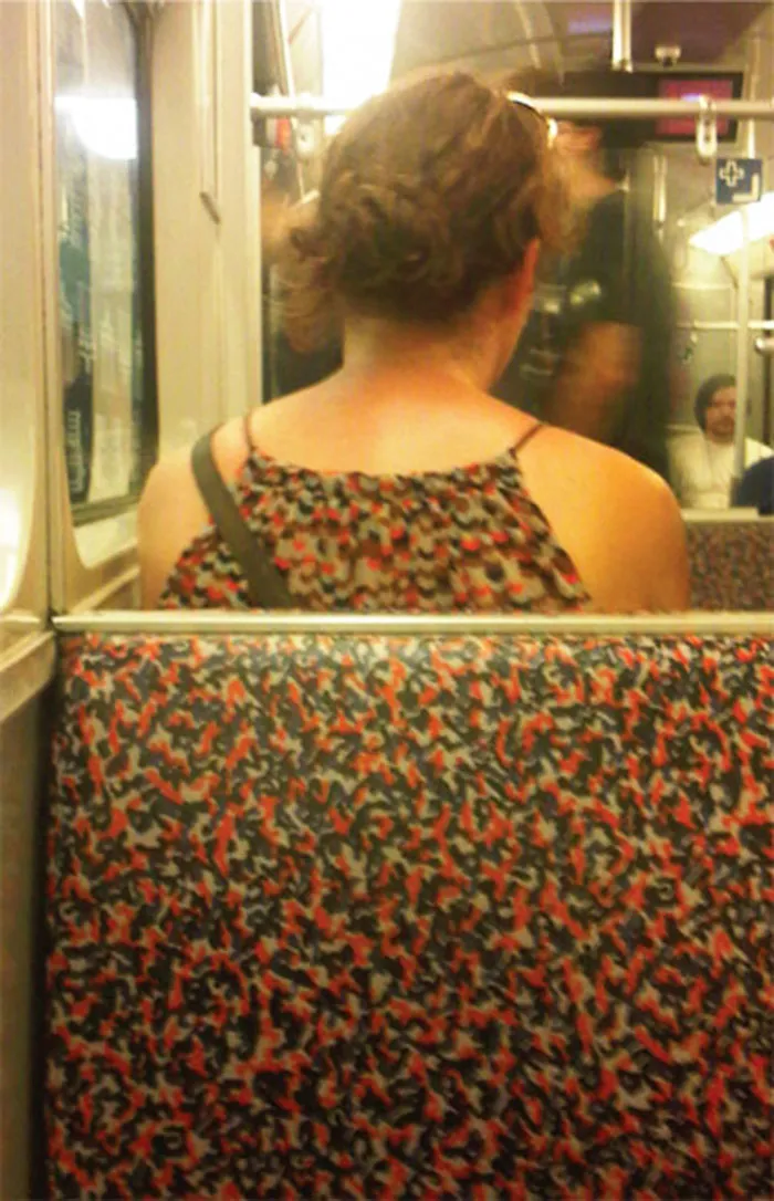Woman in a patterned dress sitting on a bus seat with matching fabric, creating a humorous visual illusion.