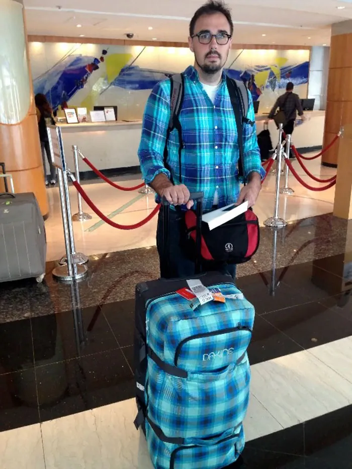 Man in a blue plaid shirt with matching luggage at a hotel lobby, embodying "who wore it better" humor.