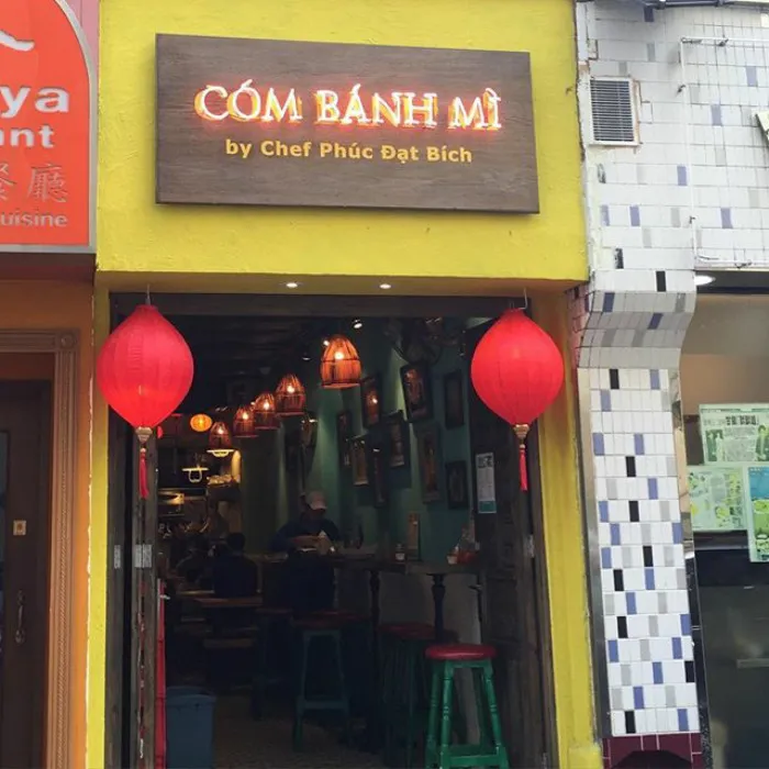 Funny restaurant sign by Chef Phuc Dat Bich, featuring bright lights and red lanterns at entrance.