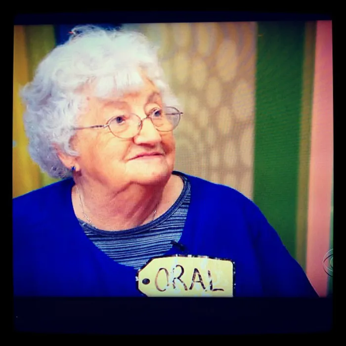 An older woman with glasses wearing a tag labeled with a funny name at a colorful event.